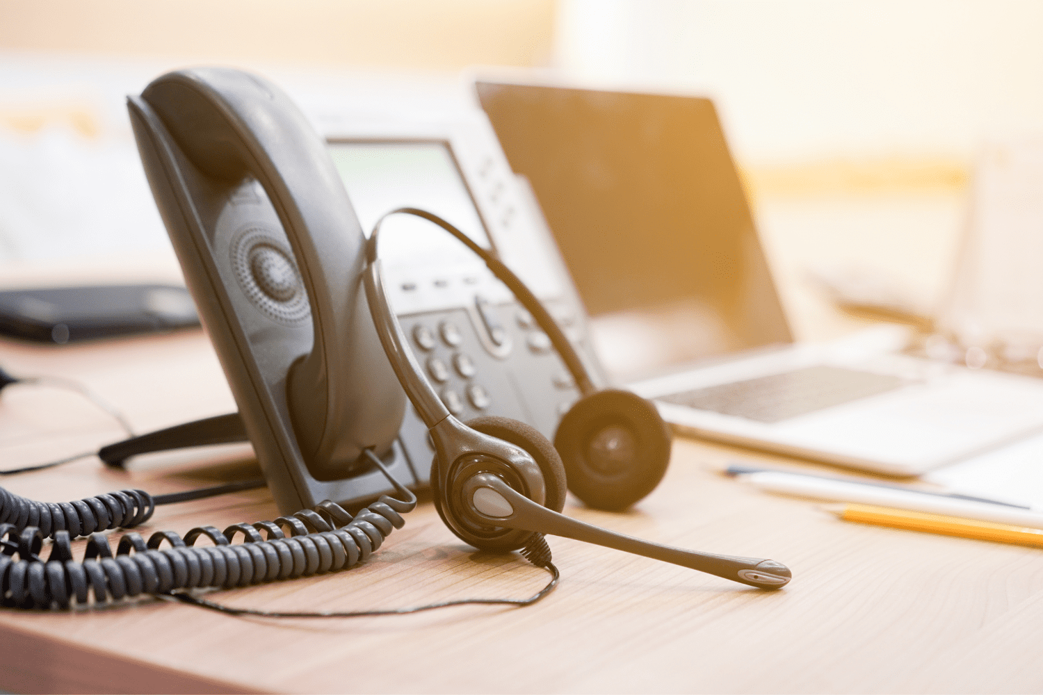 VoIP headset leaning on VoIP call center phone on a desk, next to an laptop using eDialer